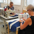 Load image into Gallery viewer, Two people working on sewing machines in a workshop setting.