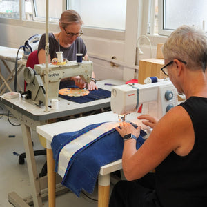 Two people working on sewing machines in a workshop setting.