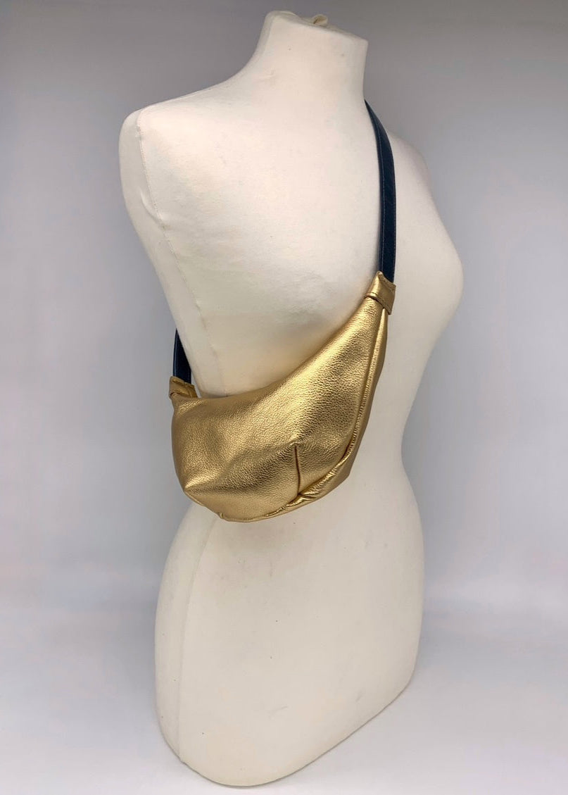 Small crossbody bag in gold leather worn across a mannequin